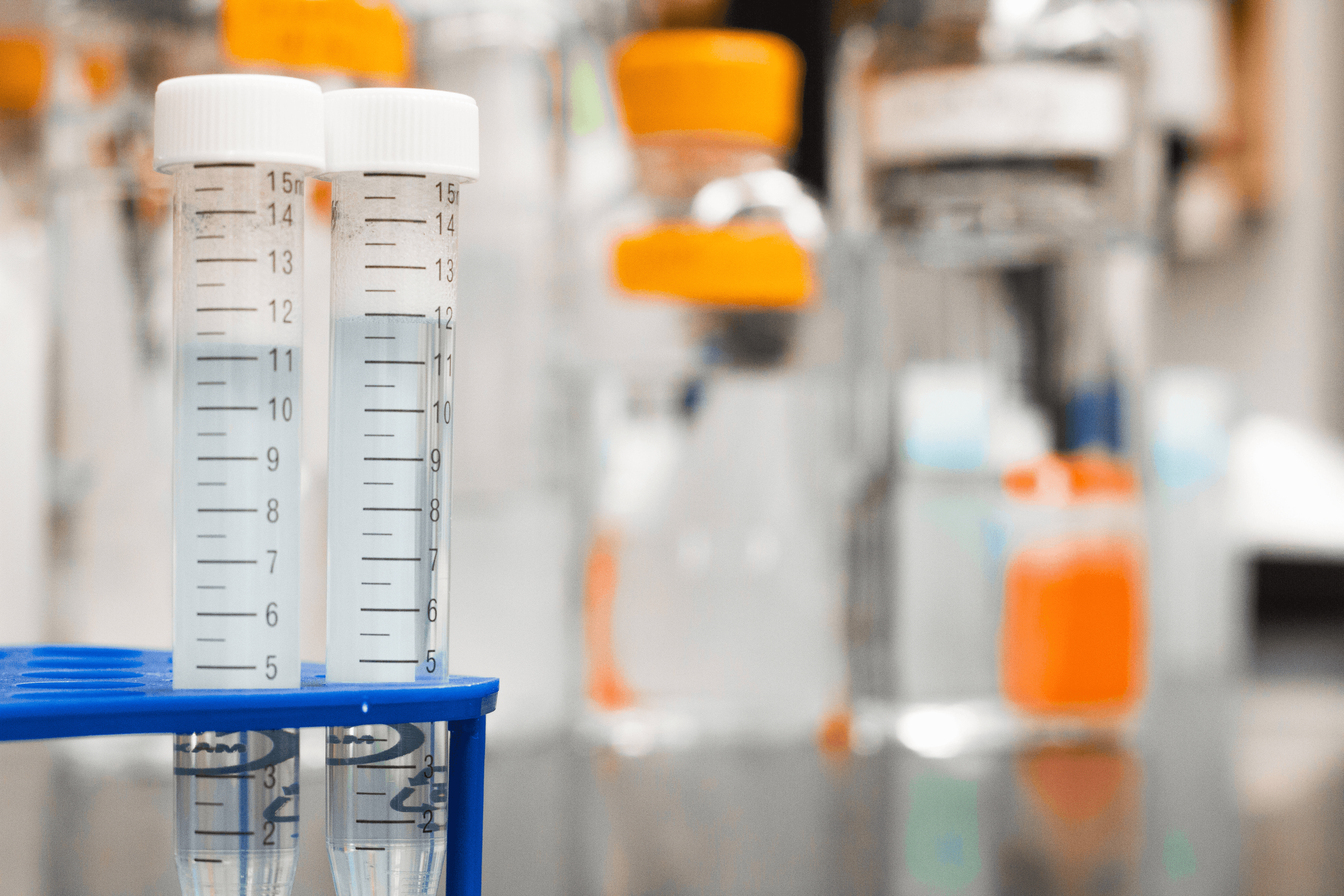 Two test tubes sit in a rack in a laboratory, near other lab equipment