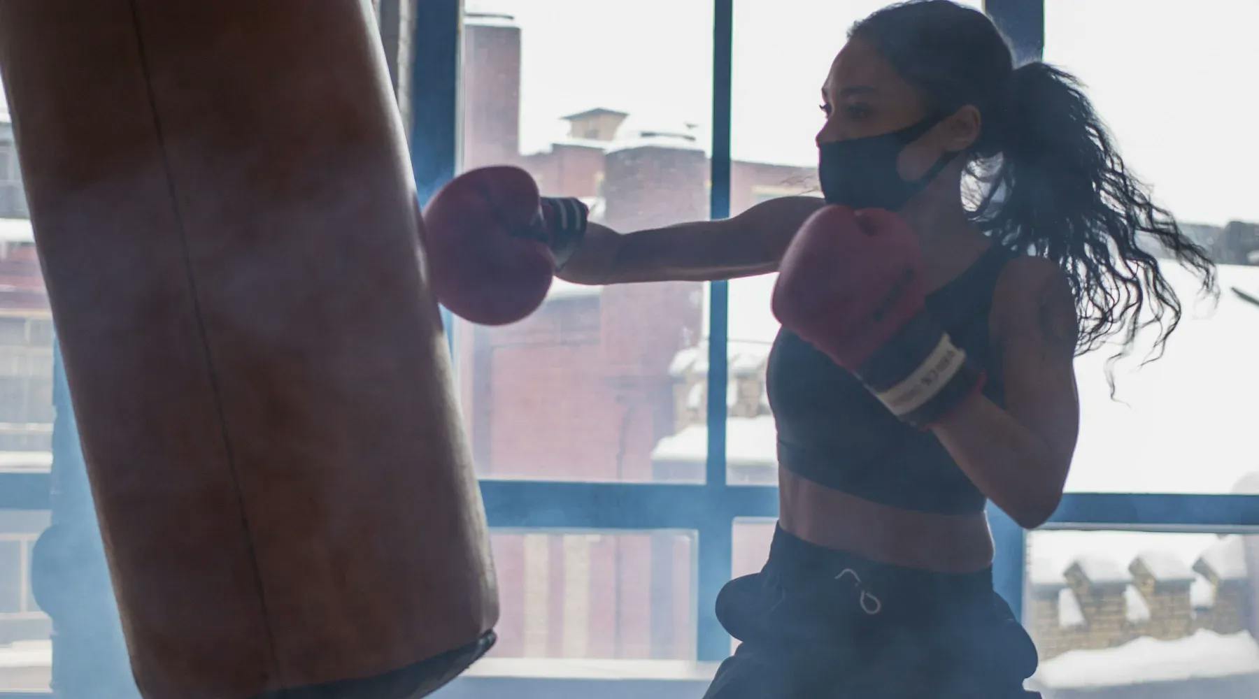 A young woman in athletic gear trains with boxing gloves and a heavy bag.